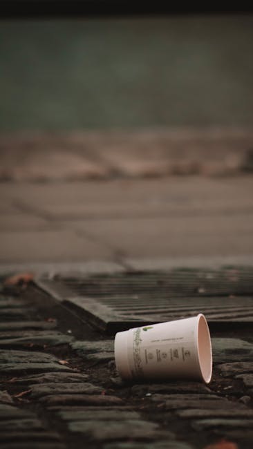 A pile of mixed waste materials is situated against a brick and block wall, consisting of flattened cardboard boxes, some partially torn or crumpled, along with a large woven textile bag that appears 